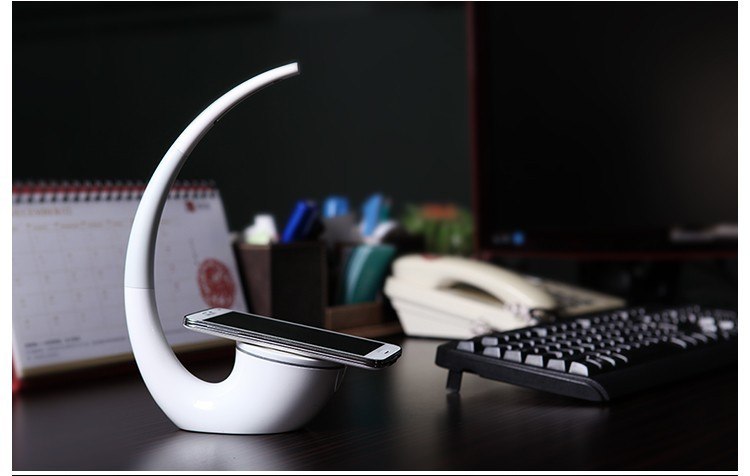 Moderne LED-Schreibtischlampe mit kabelloser Ladestation für Smartphones und platzsparendem Design.