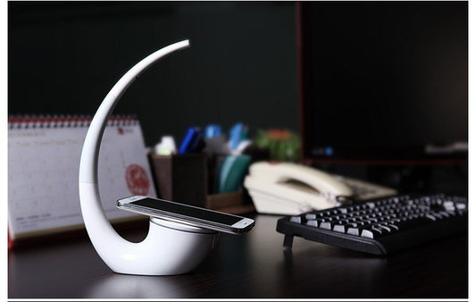 Moderne LED-Schreibtischlampe mit kabelloser Ladestation für Smartphones und platzsparendem Design.