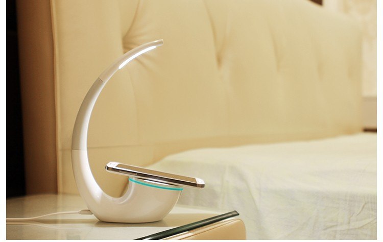 Moderne LED-Schreibtischlampe mit kabelloser Ladestation für Smartphones und platzsparendem Design.
